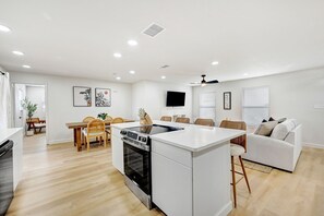 Een moderne keuken met witte kastjes, een ingebouwde oven en een eethoek met houten stoelen en een tafel.
