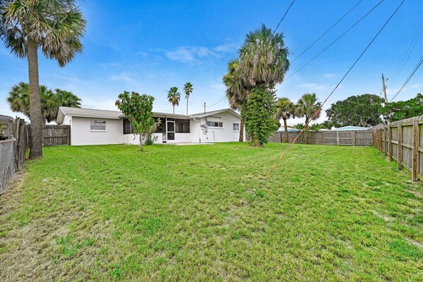 A residential property with a fenced backyard, a house with a garage, and palm trees. - Anchor14 | Coastal Getaway on Merritt Island (Merritt Island)