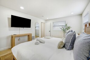 A modern hotel room with a large bed, a flat-screen TV mounted on the wall, a bedside table, and a mirror. - Anchor14 | Coastal Getaway on Merritt Island (Merritt Island)