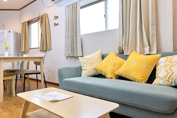 A cozy room with a light blue sofa, yellow patterned cushions, a small wooden table, and a window with curtains.