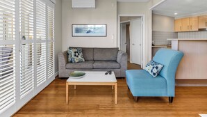 A modern living room with a grey sofa, a blue armchair, a white coffee table, and a framed picture on the wall. - The Pool Resort Kingscliff - One Bedroom (7106) - Holiday Management Co. (Tweed)