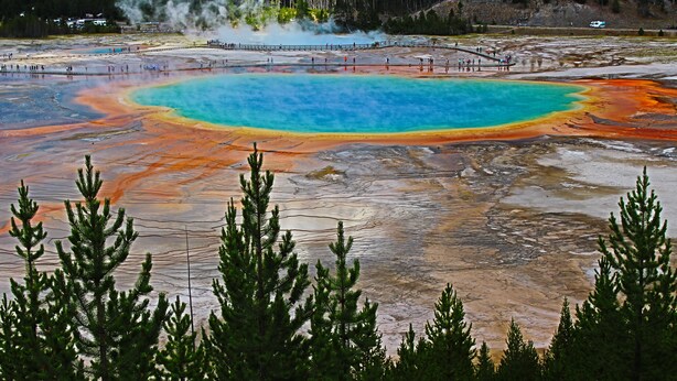 Eine geothermal erwärmte Thermalquelle mit einem türkisblauen Zentrum, umgeben von orange- und braunen Ablagerungen aus Mineralien.