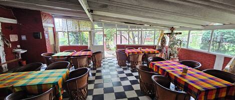 A restaurant with checkered flooring, wooden chairs, and tables covered with colorful tablecloths.