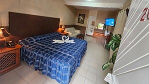Una habitación de hotel con una cama grande, una mesita de noche con lámpara, un televisor y un refrigerador.