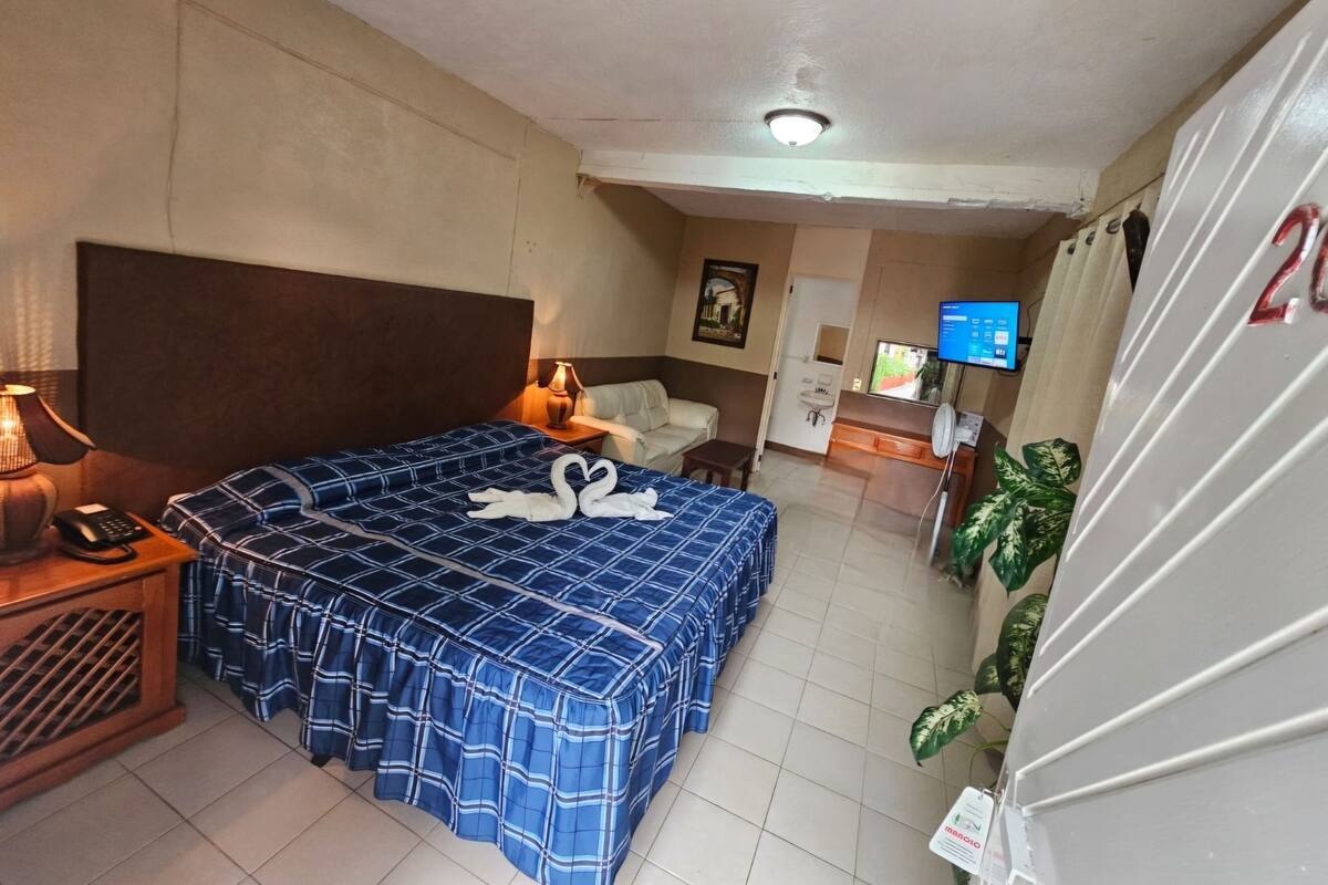 Una habitación de hotel con una cama grande, una mesita de noche con lámpara, un televisor y un refrigerador.