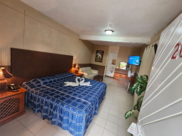 Una habitación de hotel con una cama grande, una mesita de noche con lámpara, un televisor y un refrigerador.