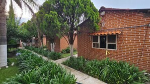Un edificio de ladrillo con tejado de tejas, rodeado de exuberante vegetación y un jardín bien cuidado.