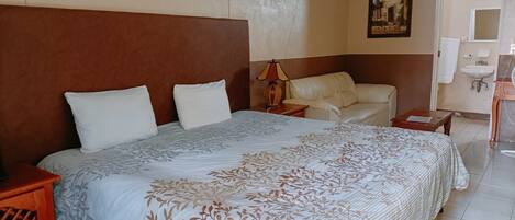 Habitación de hotel con una cama grande, un sofá, una mesita y un baño visible a través de una puerta abierta.