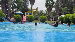 Un área de piscina con tobogán, palmeras y una estructura acuática.
