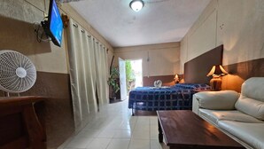 Habitación de hotel con cama, sofá, mesa de madera, televisor, ventilador y lámpara.