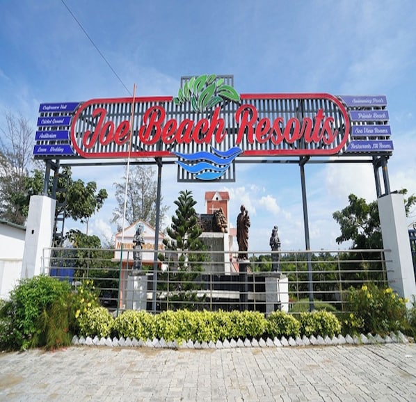 A sign for The Beach Resorts with a palm tree logo, a statue, and a fence. - Joe Beach Resort (Tirupporur)