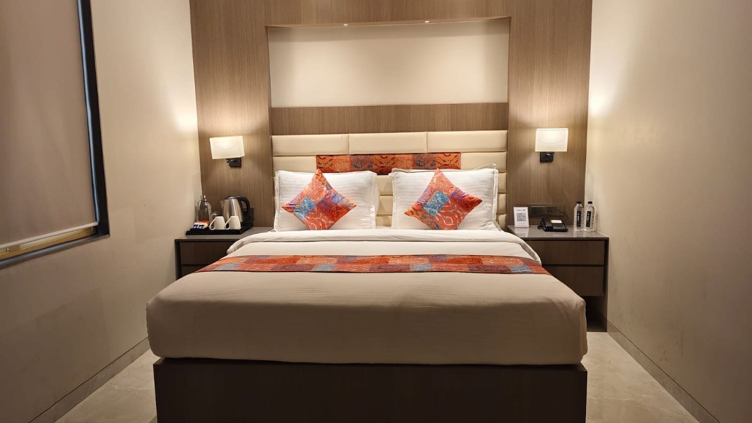 Une chambre d’hôtel avec un grand lit, deux tables de chevet, une tête de lit et des lampes fixées au mur.
