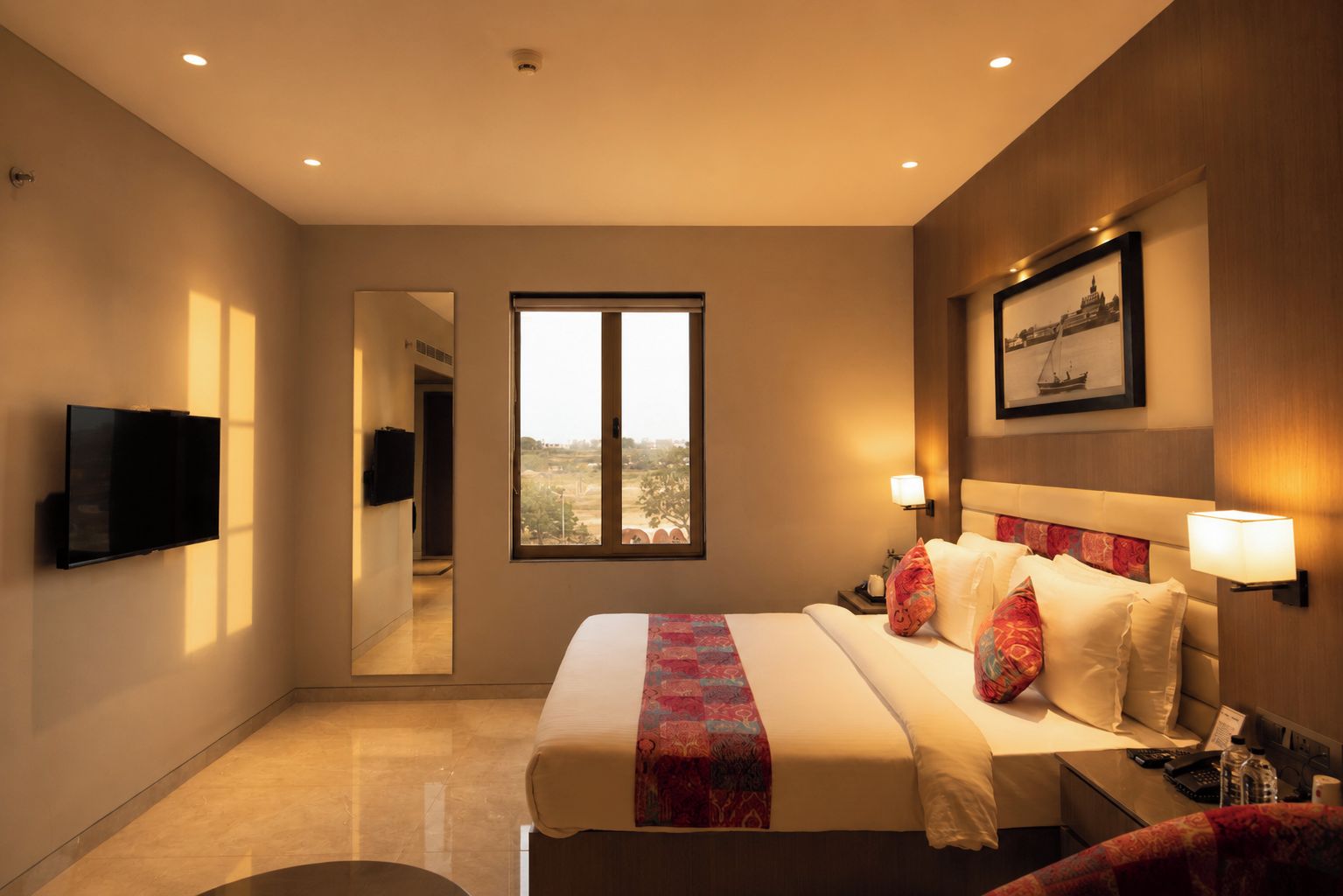 Una camera d'albergo con un letto, lampade da comodino, una televisione a schermo piatto, una grande finestra e un quadro appeso al muro.