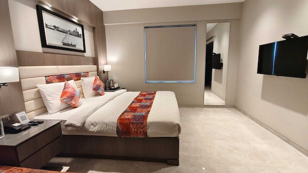 A hotel room with a bed, bedside table, lamp, and a TV mounted on the wall. - LA CASA DE RANN (Bhuj)