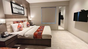 A hotel room with a bed, bedside table, lamp, and a TV mounted on the wall.
