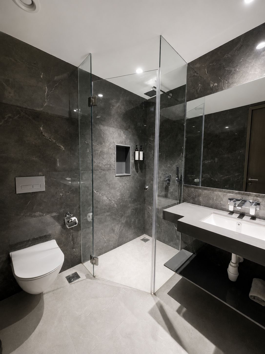 Une salle de bain moderne avec une douche à parois de verre, des toilettes blanches et un grand miroir au-dessus d’un lavabo.