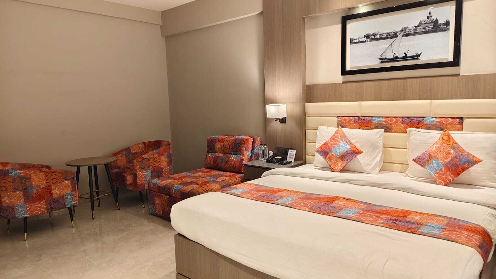 Habitación de hotel con cama, dos sillones, una mesita, una mesita de noche y un cuadro colgado en la pared.
