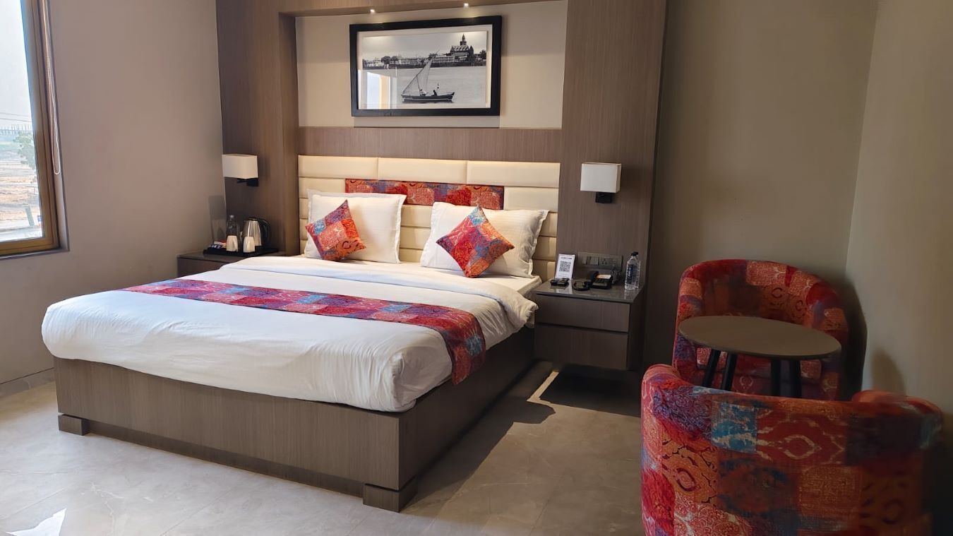 A hotel room with a large bed, two bedside tables, a chair, a framed picture on the wall, and a window.
