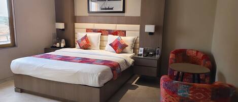 A hotel room with a large bed, two bedside tables, a chair, a framed picture on the wall, and a window.