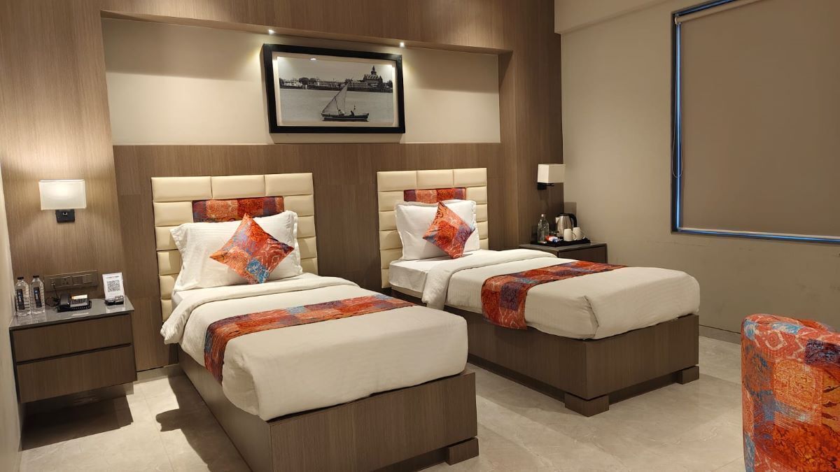 A hotel room with two beds, a nightstand, a chair, a framed picture on the wall, and a projector screen.