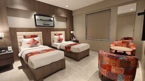 A hotel room with two beds, a sofa, a small table, and a large window. - LA CASA DE RANN (Bhuj)