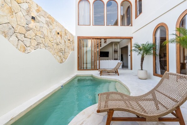 Un espace piscine moderne avec un mur en pierre, un fauteuil de relaxation et une plante en pot.