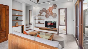 A modern living room with a sofa, coffee table, TV, wooden shelves, and a ceiling fan. - deTasia Villa by Kozystay - Jimbaran (Jimbaran)