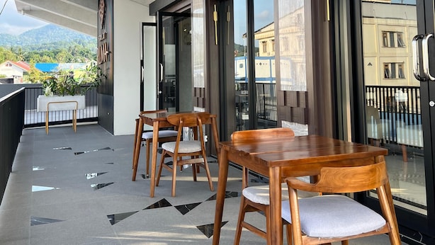 A modern outdoor seating area with wooden tables and chairs, large windows, and a view of the cityscape. - RUMA GUEST HOUSE (Kotabaru)