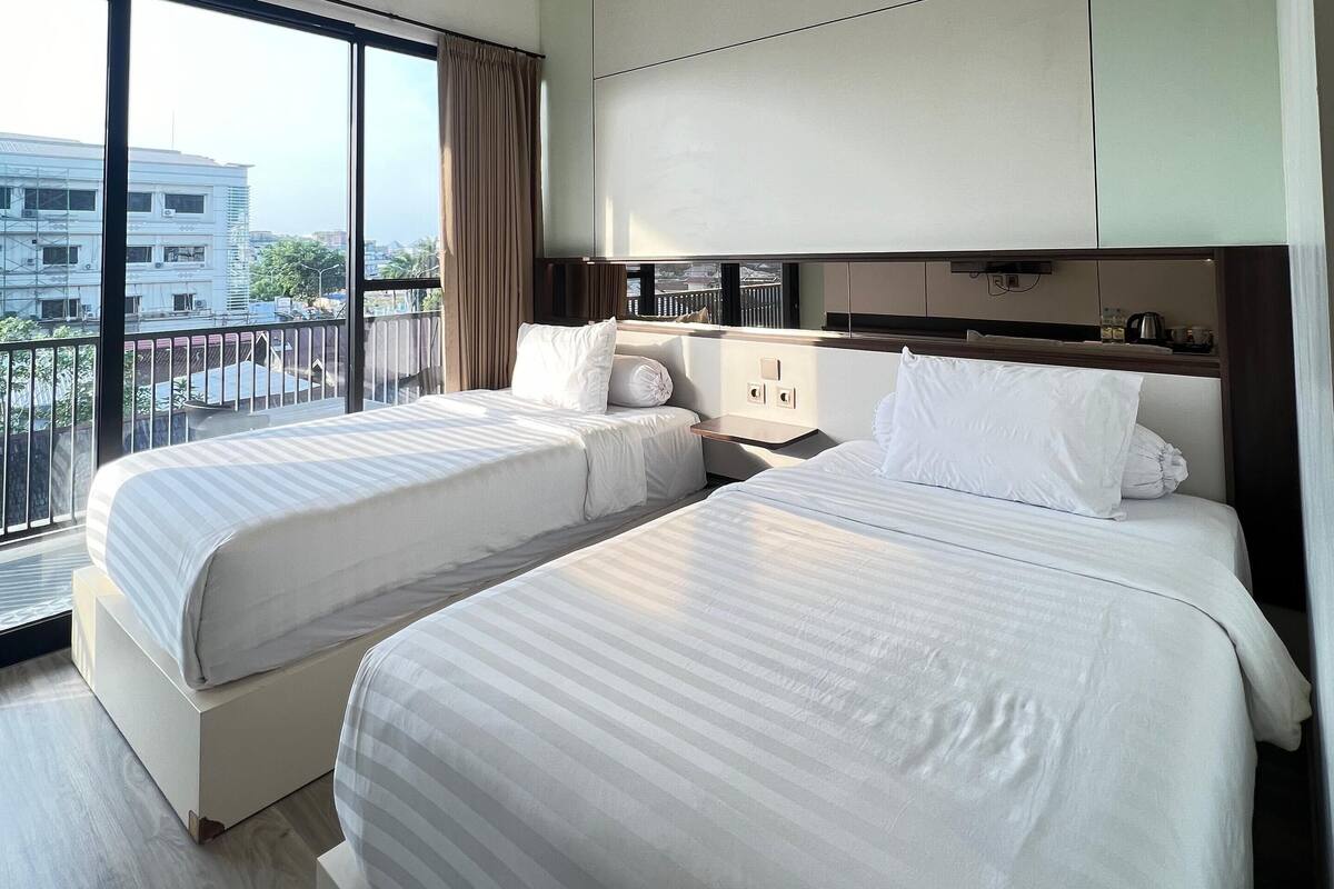 A hotel room with two beds, a large window, and a view of buildings.