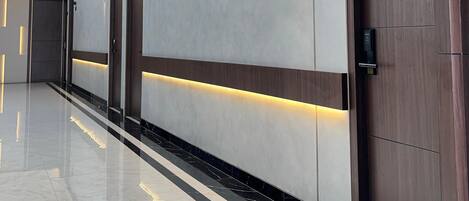A modern hallway with a polished floor, a skylight, and a series of doors with illuminated numbers.