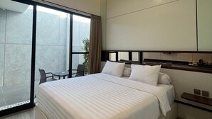 A modern hotel room with a large bed, a sliding glass door to a balcony, and a small table with chairs. - RUMA GUEST HOUSE (Kotabaru)