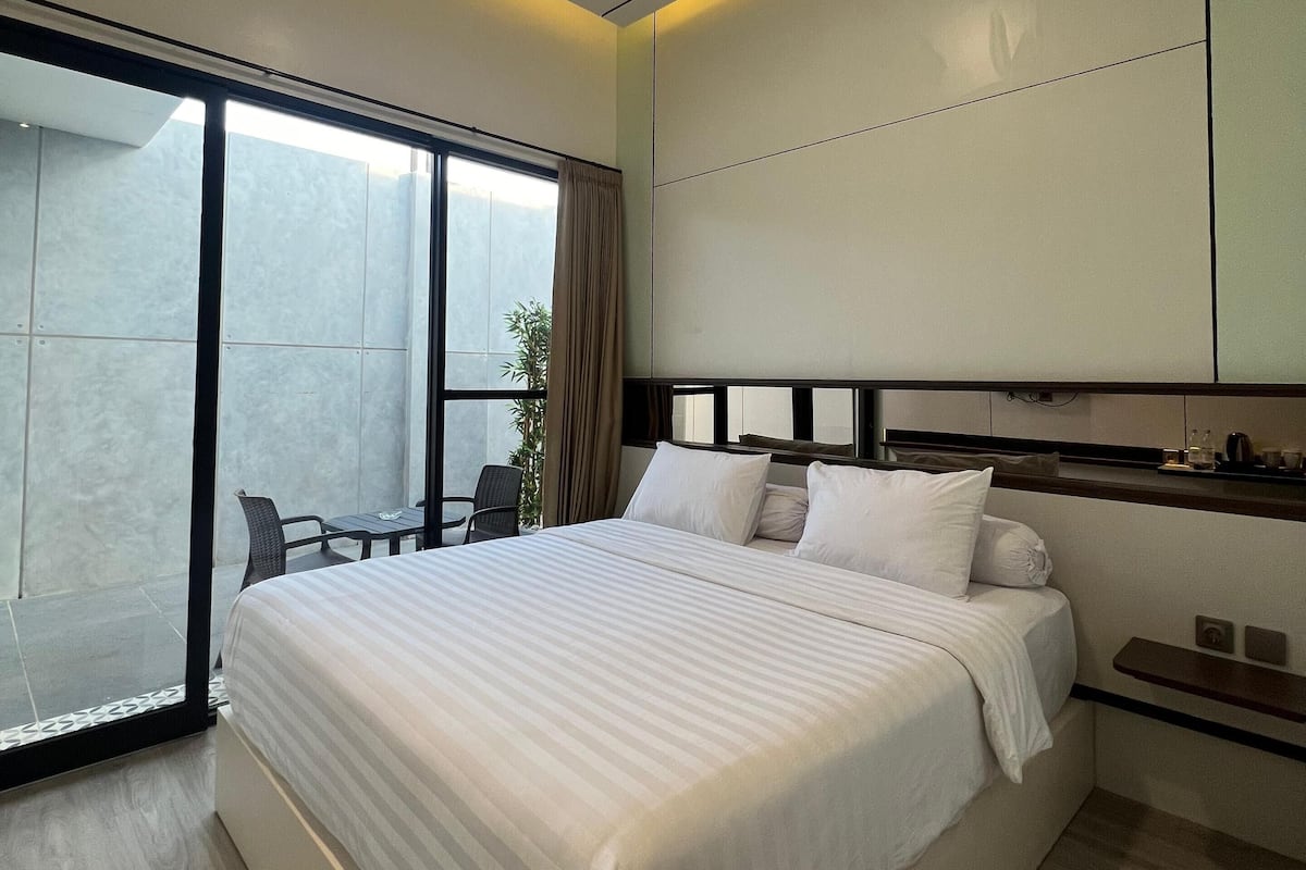 A modern hotel room with a large bed, a sliding glass door to a balcony, and a small table with chairs.