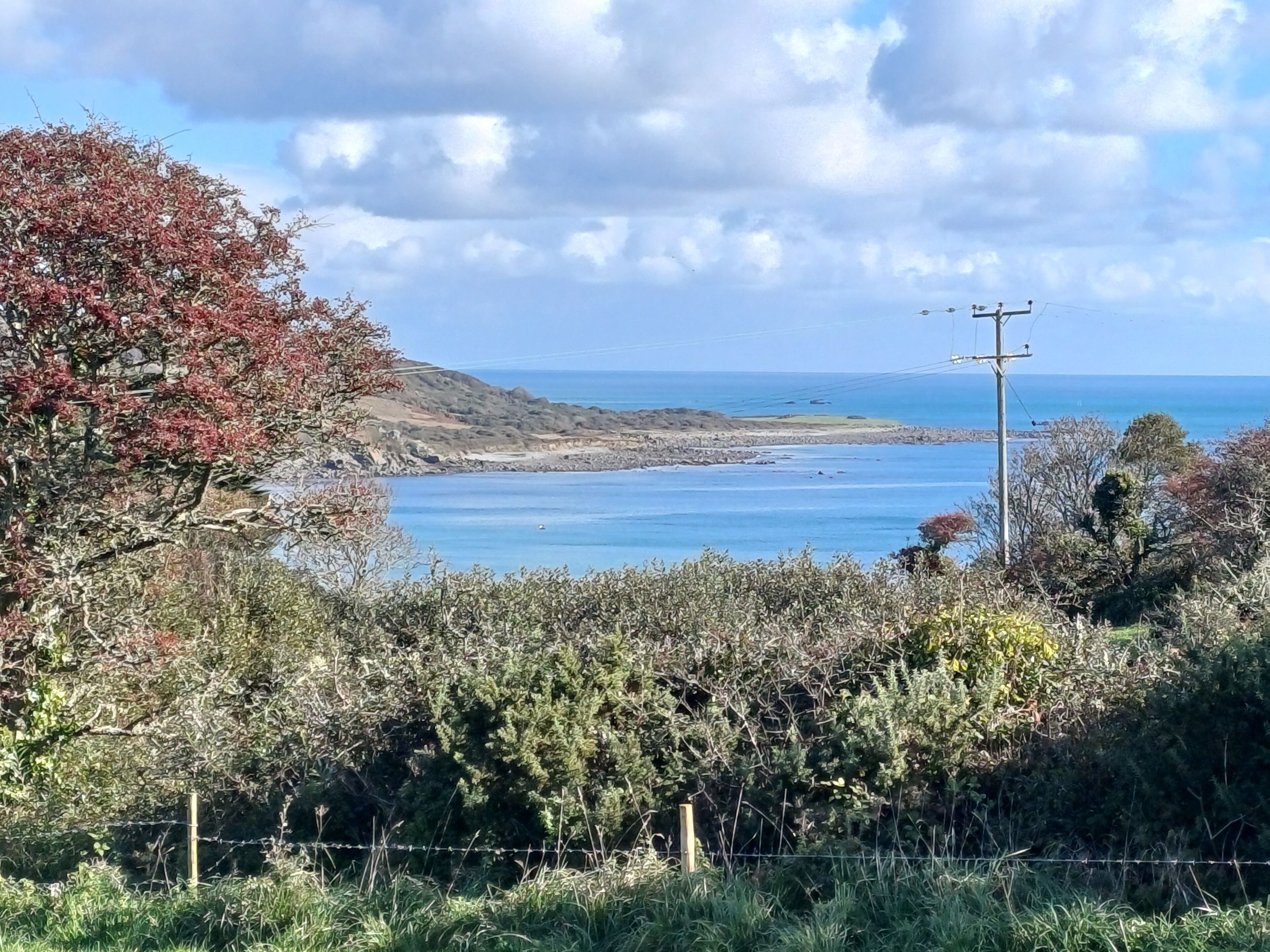 Un paisaje costero con vista despejada al mar, una colina con vegetación escasa y un poste de electricidad.