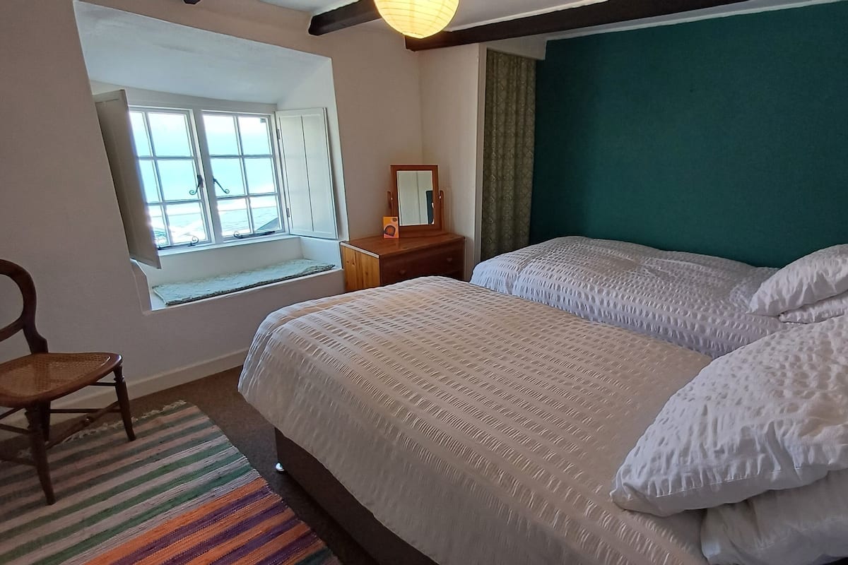 A bedroom with two beds, a window with a view, a chair, and a bedside table.