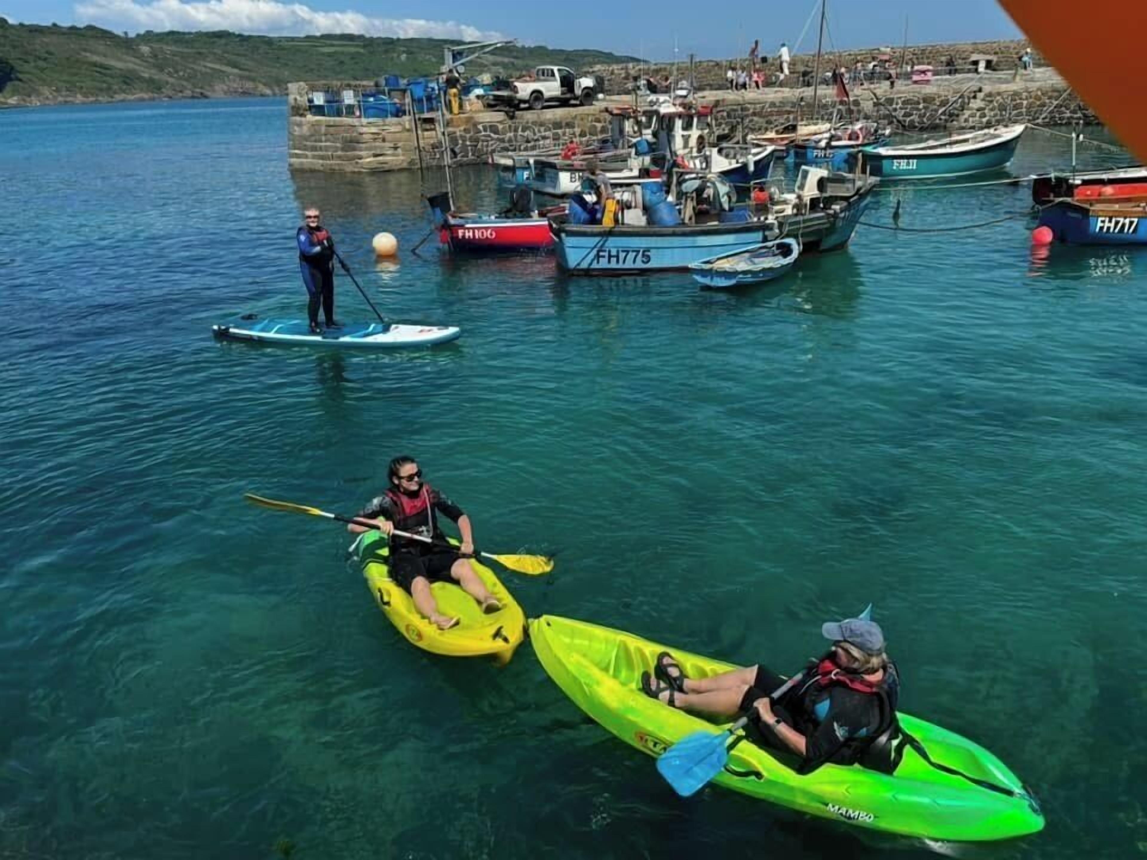 A calm water body with kayaks and a paddleboard. Boats are docked in the background.