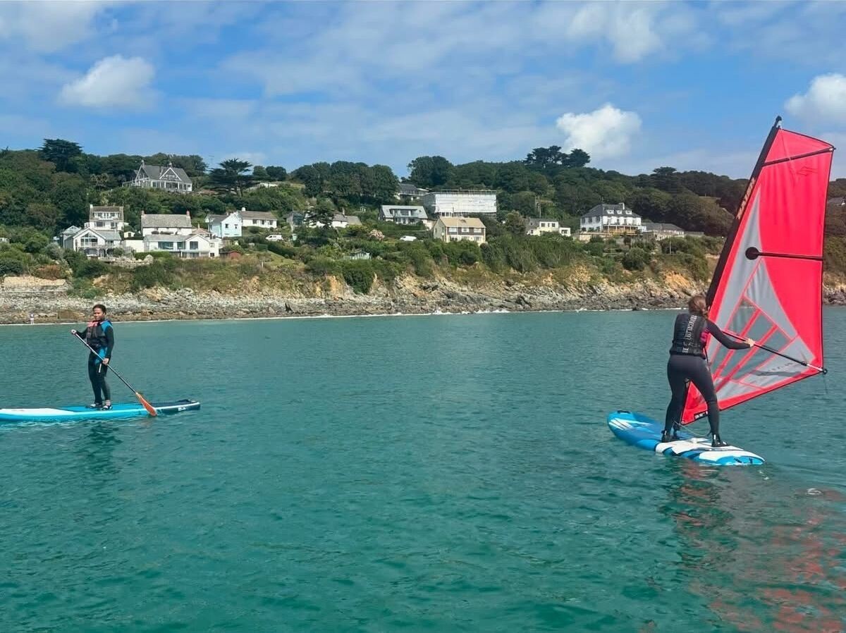 Due persone su tavole da paddleboard in acque calme, con case sullo sfondo.
