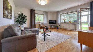 Ein Wohnzimmer mit einer Couch, einem Couchtisch, einem Fernseher und einem großen Fenster mit Vorhängen.