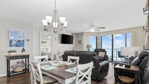A modern living room with a dining table, white chairs, a black leather sofa, and a ceiling fan. - Oceanfront Luxury 4BR | Sleeps 10 | Beach Club II (North Myrtle Beach)