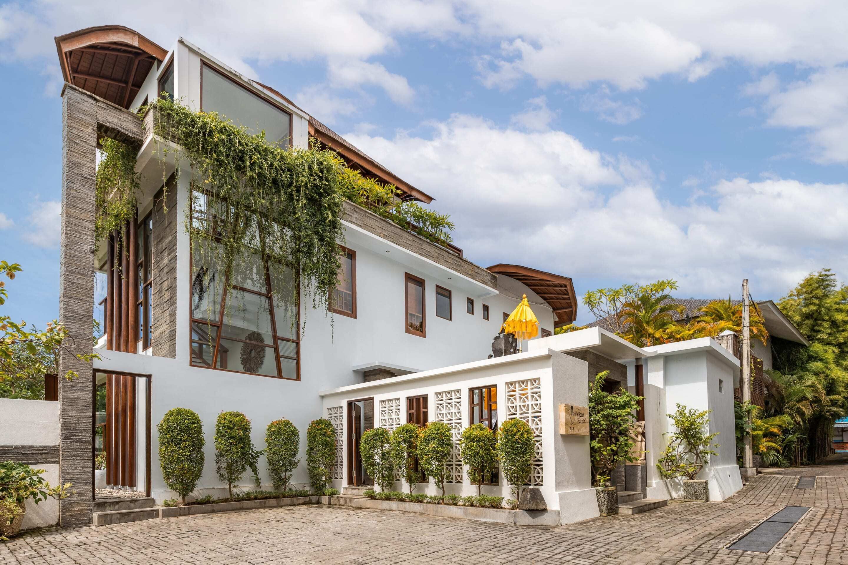 Ein modernes, zweistöckiges Haus mit heller Fassade, großen Fenstern und einem mit Grünpflanzen bepflanzten Balkon.