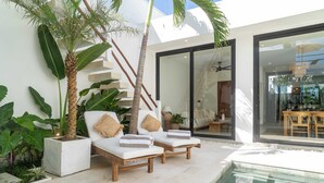 A modern outdoor pool area with lounge chairs and a palm tree. - Villa Lu'um (Canggu)