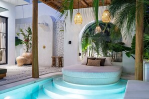 Un espacio circular de estar al aire libre con piscina, rodeado de plantas y un muro de piedra.