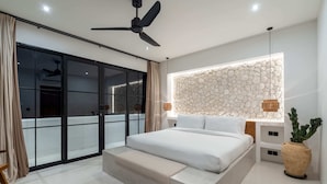 A modern bedroom with a large bed, a ceiling fan, a stone wall, and a large window. - Villa Irie (Cemagi)