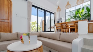 A modern living room with a sofa, a round table, and a dining area with chairs. - Villa Delia (Munggu)