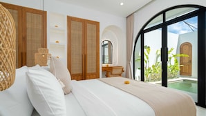 A bedroom with a large bed, a wicker chair, and a view of a swimming pool. - Villa Delia (Munggu)
