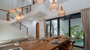 A modern dining area with a wooden table, chairs, and hanging wicker lights. - Villa Delia (Munggu)