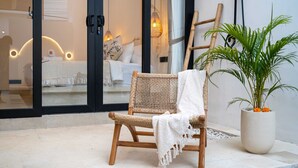 Una silla de mimbre con una manta blanca, una planta en maceta con flores anaranjadas y un ambiente junto a la piscina.