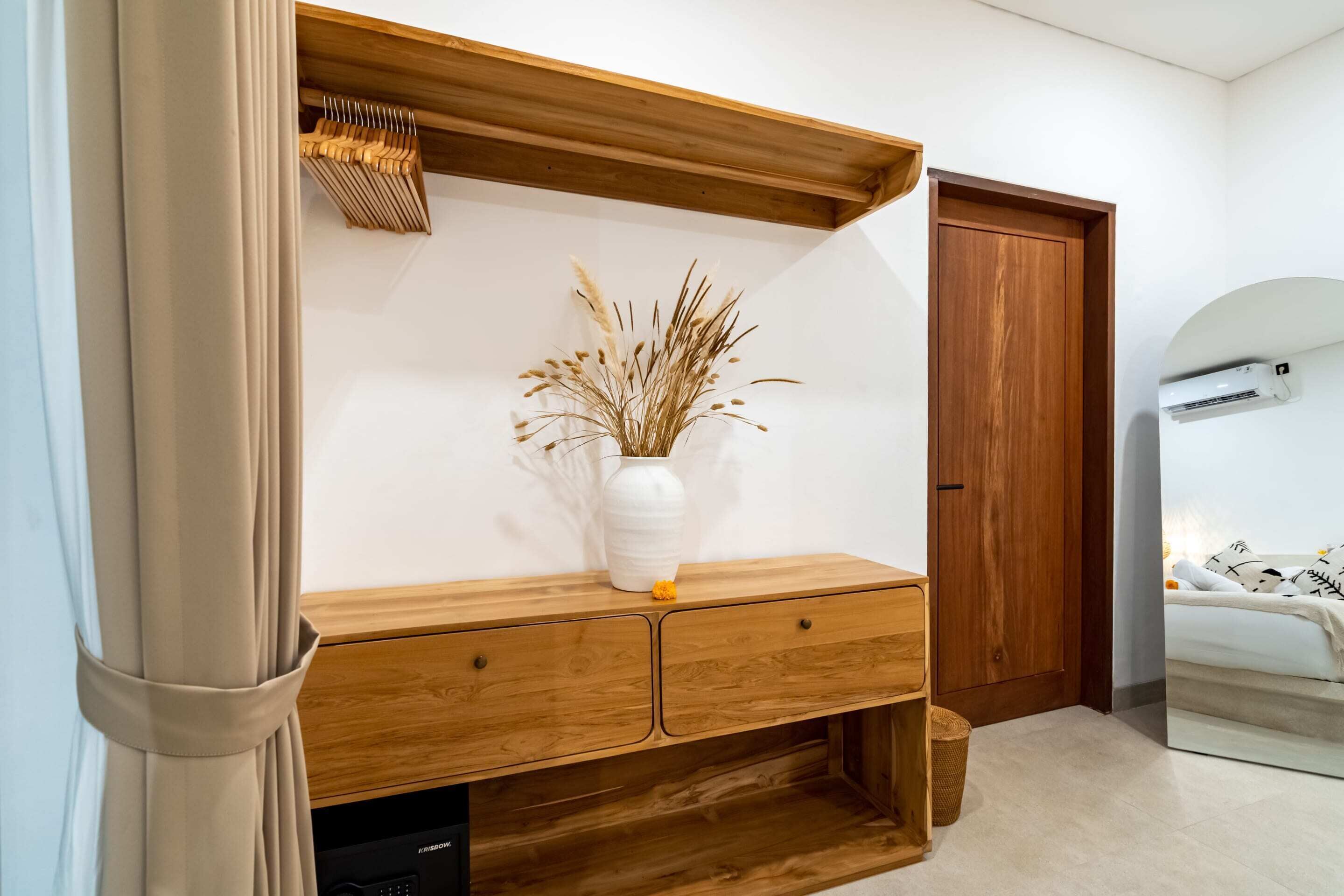 Um aparador de madeira com um vaso de plantas secas, uma porta de madeira e uma parede branca.