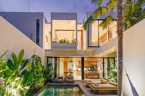 Un immeuble résidentiel moderne à plusieurs niveaux, doté d’une piscine, d’un espace extérieur aménagé et d’une végétation luxuriante.