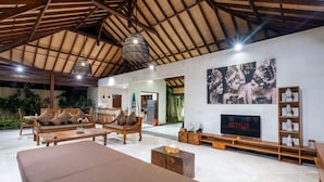Un amplio espacio habitable con techo alto, muebles de madera, un televisor y un estante de pared con objetos decorativos.