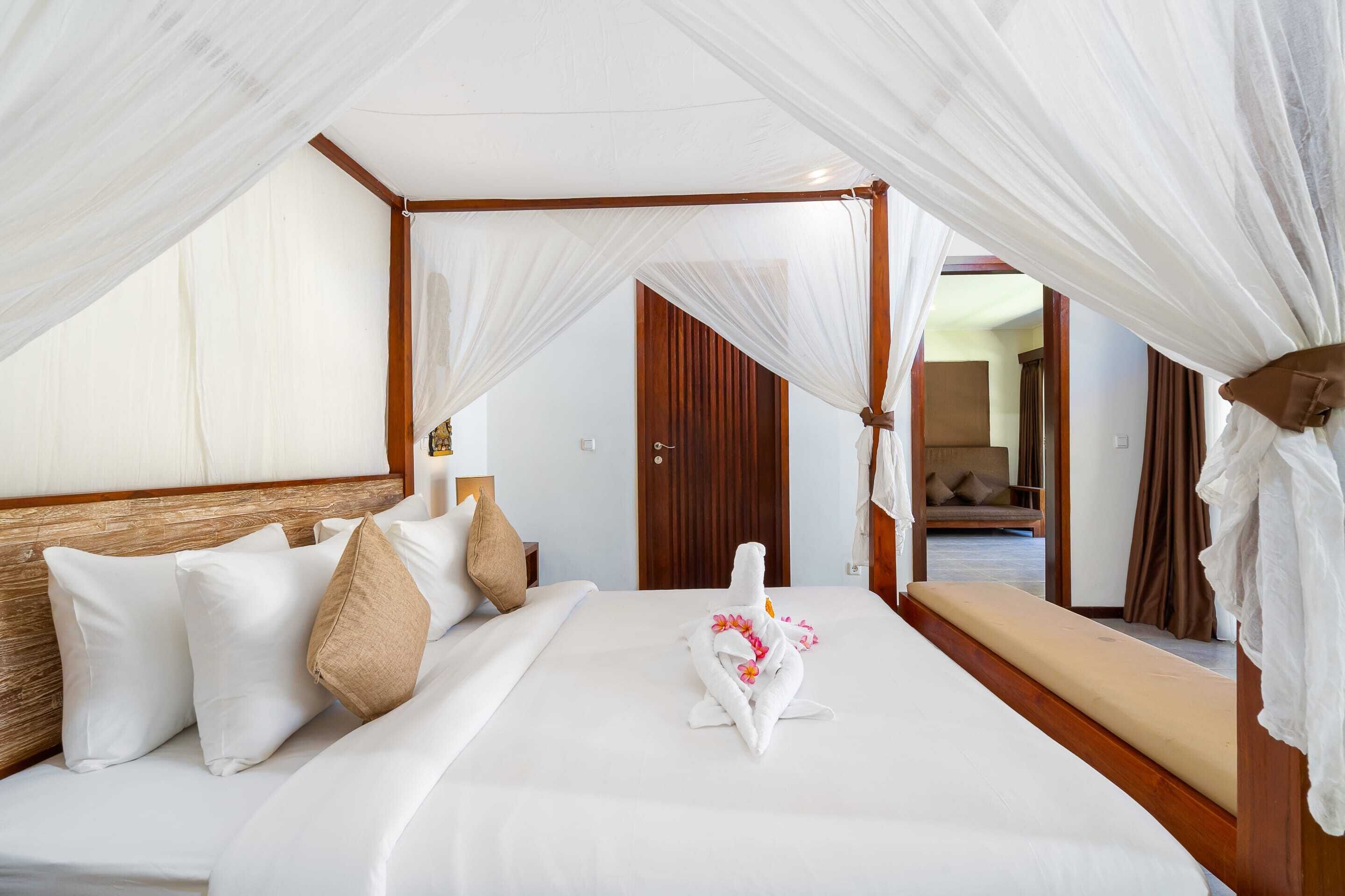 A hotel room with a canopy bed, a wooden headboard, and a bench with a cushion.
